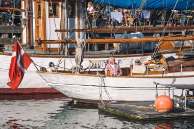 Kopenhag, Danimarka - 23 Mayıs 2022: Kopenhag 'da 17. yüzyıl kıyısı, kanal ve eğlence bölgesi Nyhavn Kanalı veya Yeni Liman boyunca Danimarka bayrağı ve yerel halk taşıyan eski ahşap tekne