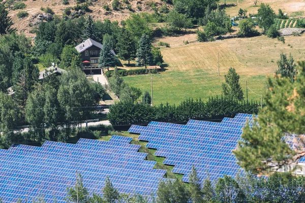 Aerial view of solar panels in the field in the countryside with house and cultivation on background. Solar power plant. Blue solar panels. Alternative source