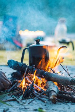 Preparing coffee or tea on an bonfire with branches and flames outdoor in the nature, vertical