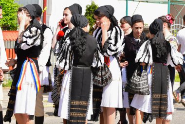 Geleneksel siyah motiflerle dikilmiş ulusal keten pastoral kostümlü Romen halk dansçıları, geleneksel siyah şapka giyen erkekler ve püsküllü siyah fular giyen kadınlar