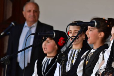 Geleneksel siyah motiflerle dikilmiş ulusal keten pastoral kostümlü Romen halk dansçıları, geleneksel siyah şapka giyen erkekler ve püsküllü siyah fular giyen kadınlar