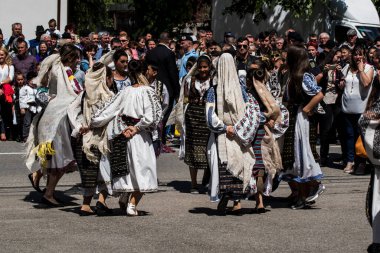 Geleneksel siyah motiflerle dikilmiş ulusal keten pastoral kostümlü Romen halk dansçıları, geleneksel siyah şapka giyen erkekler ve püsküllü siyah fular giyen kadınlar