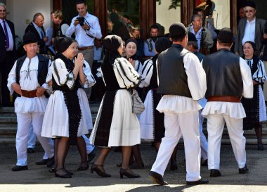 Geleneksel siyah motiflerle dikilmiş ulusal keten pastoral kostümlü Romen halk dansçıları, geleneksel siyah şapka giyen erkekler ve püsküllü siyah fular giyen kadınlar