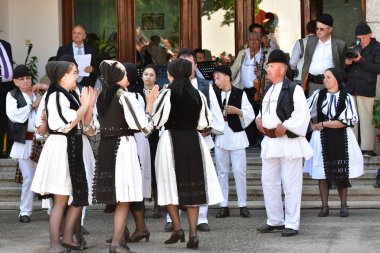 Geleneksel siyah motiflerle dikilmiş ulusal keten pastoral kostümlü Romen halk dansçıları, geleneksel siyah şapka giyen erkekler ve püsküllü siyah fular giyen kadınlar