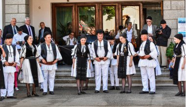 Geleneksel siyah motiflerle dikilmiş ulusal keten pastoral kostümlü Romen halk dansçıları, geleneksel siyah şapka giyen erkekler ve püsküllü siyah fular giyen kadınlar