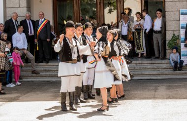 Geleneksel siyah motiflerle dikilmiş ulusal keten pastoral kostümlü Romen halk dansçıları, geleneksel siyah şapka giyen erkekler ve püsküllü siyah fular giyen kadınlar