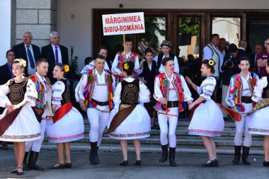 Transilvanya 'dan halk dansçıları tavus kuşu boncukları ve tüyleriyle süslenmiş astrakhan kuzu derisi şapkalar giyer, beyaz keten gömlek ve pantolon, geniş deri kemer, ulusal bayrağı temsil eden üç renkli köşegen.