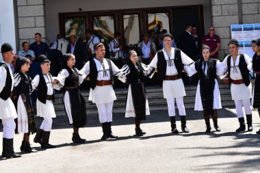 Geleneksel siyah motiflerle dikilmiş ulusal keten pastoral kostümlü Romen halk dansçıları, geleneksel siyah şapka giyen erkekler ve püsküllü siyah fular giyen kadınlar
