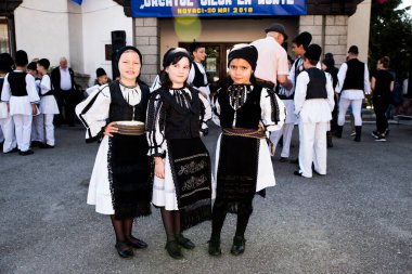 Geleneksel siyah motiflerle dikilmiş ulusal keten pastoral kostümlü Romen halk dansçıları, geleneksel siyah şapka giyen erkekler ve püsküllü siyah fular giyen kadınlar