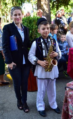 Romanya 'da Novaci' li bir çocuk ulusal keten çoban kostümü giymiş, geleneksel siyah motifler takmış ve siyah bir şapka takıyor.