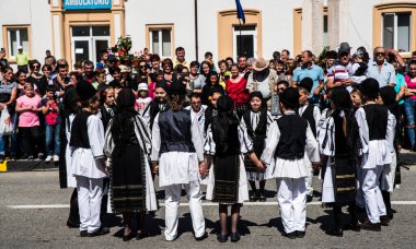 Geleneksel siyah motiflerle dikilmiş ulusal keten pastoral kostümlü Romen halk dansçıları, geleneksel siyah şapka giyen erkekler ve püsküllü siyah fular giyen kadınlar