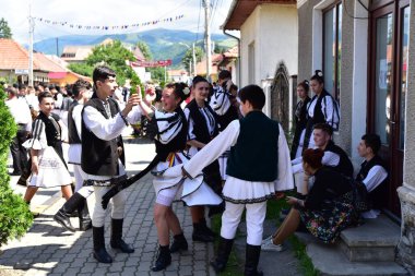 Geleneksel siyah motiflerle dikilmiş ulusal keten pastoral kostümlü Romen halk dansçıları, geleneksel siyah şapka giyen erkekler ve püsküllü siyah fular giyen kadınlar