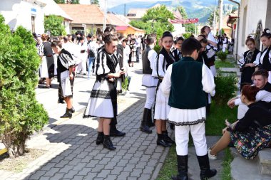 Geleneksel siyah motiflerle dikilmiş ulusal keten pastoral kostümlü Romen halk dansçıları, geleneksel siyah şapka giyen erkekler ve püsküllü siyah fular giyen kadınlar