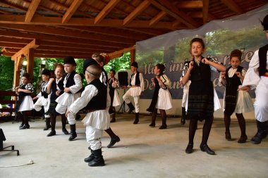 Geleneksel siyah motiflerle dikilmiş ulusal keten pastoral kostümlü Romen halk dansçıları, geleneksel siyah şapka giyen erkekler ve püsküllü siyah fular giyen kadınlar