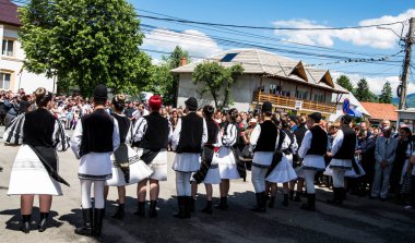 Geleneksel siyah motiflerle dikilmiş ulusal keten pastoral kostümlü Romen halk dansçıları, geleneksel siyah şapka giyen erkekler ve püsküllü siyah fular giyen kadınlar
