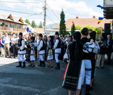 Geleneksel siyah motiflerle dikilmiş ulusal keten pastoral kostümlü Romen halk dansçıları, geleneksel siyah şapka giyen erkekler ve püsküllü siyah fular giyen kadınlar