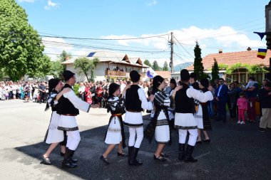 Geleneksel siyah motiflerle dikilmiş ulusal keten pastoral kostümlü Romen halk dansçıları, geleneksel siyah şapka giyen erkekler ve püsküllü siyah fular giyen kadınlar