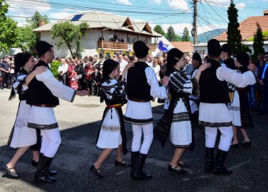 Geleneksel siyah motiflerle dikilmiş ulusal keten pastoral kostümlü Romen halk dansçıları, geleneksel siyah şapka giyen erkekler ve püsküllü siyah fular giyen kadınlar
