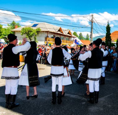 Geleneksel siyah motiflerle dikilmiş ulusal keten pastoral kostümlü Romen halk dansçıları, geleneksel siyah şapka giyen erkekler ve püsküllü siyah fular giyen kadınlar