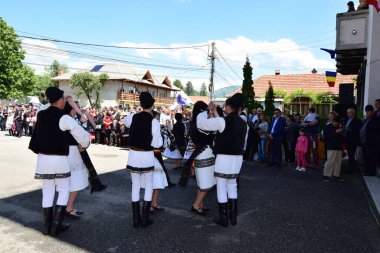 Geleneksel siyah motiflerle dikilmiş ulusal keten pastoral kostümlü Romen halk dansçıları, geleneksel siyah şapka giyen erkekler ve püsküllü siyah fular giyen kadınlar