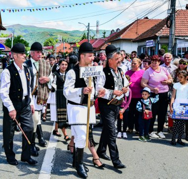 Geleneksel siyah motiflerle dikilmiş ulusal keten pastoral kostümlü Romen halk dansçıları, geleneksel siyah şapka giyen erkekler ve püsküllü siyah fular giyen kadınlar