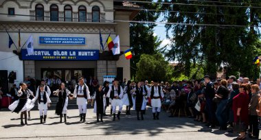 Geleneksel siyah motiflerle dikilmiş ulusal keten pastoral kostümlü Romen halk dansçıları, geleneksel siyah şapka giyen erkekler ve püsküllü siyah fular giyen kadınlar