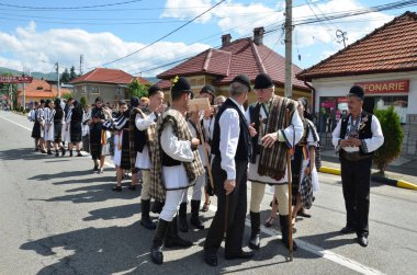 Geleneksel siyah motiflerle dikilmiş ulusal keten pastoral kostümlü Romen halk dansçıları, geleneksel siyah şapka giyen erkekler ve püsküllü siyah fular giyen kadınlar