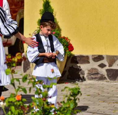 Sibiu Romania çayır çocuğu ulusal keten çoban kostümü giymiş, geleneksel siyah motiflerle dikilmiş, etek, pantolon, geniş deri kemer, göğüs ve siyah pastoral şapka ve üç renkli atkıdan oluşan bir gömlek giyiyor..