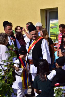 Geleneksel siyah motiflerle dikilmiş ulusal çoban elbisesi giymiş, Romanya 'da bir belediye başkanı, yuvarlak siyah bir şapka, geniş bir deri kimir ve belediye başkanı için üç renkli bir eşarp giyiyor.