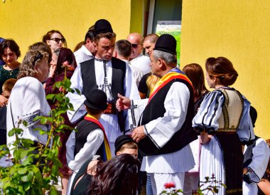 Geleneksel siyah motiflerle dikilmiş ulusal çoban elbisesi giymiş, Romanya 'da bir belediye başkanı, yuvarlak siyah bir şapka, geniş bir deri kimir ve belediye başkanı için üç renkli bir eşarp giyiyor.