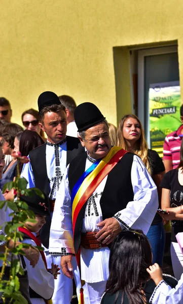 Geleneksel siyah motiflerle dikilmiş ulusal çoban elbisesi giymiş, Romanya 'da bir belediye başkanı, yuvarlak siyah bir şapka, geniş bir deri kimir ve belediye başkanı için üç renkli bir eşarp giyiyor.