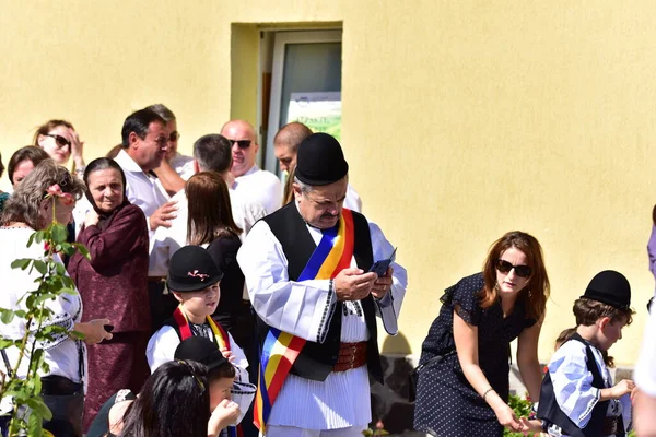 Geleneksel siyah motiflerle dikilmiş ulusal çoban elbisesi giymiş, Romanya 'da bir belediye başkanı, yuvarlak siyah bir şapka, geniş bir deri kimir ve belediye başkanı için üç renkli bir eşarp giyiyor.