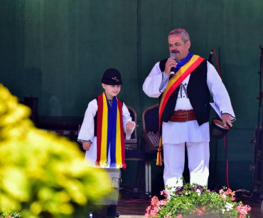 Geleneksel siyah motiflerle dikilmiş ulusal çoban elbisesi giymiş, Romanya 'da bir belediye başkanı, yuvarlak siyah bir şapka, geniş bir deri kimir ve belediye başkanı için üç renkli bir eşarp giyiyor.