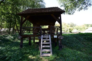 Manual mill or mill for corn flour consisting of two millstones with central wooden handle, supported by a bar between two logs on a two-legged support, with four soles at ground level