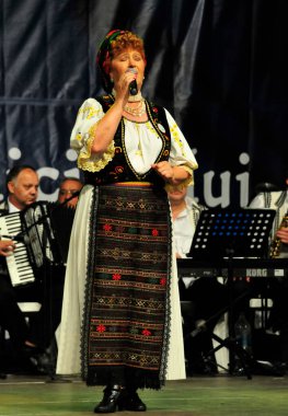 Tarnavelor vadisinden bir sanatçı. Kromatiklik az renk içerir. Kadın giysileri yaka ve ia, bileklerinden toplanmış geniş kollar ve siyah iplikle bitirilmiş bir fırça ile bitirdi.