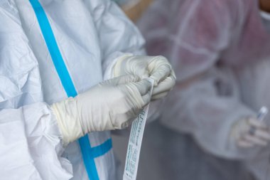 PPE giysisi olan doktor, nazal çubuk ile ATK test kiti kullanan bir test koronavirüsü (covid-19) kullanıyor..