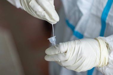 PPE giysisi olan doktor, nazal çubuk ile ATK test kiti kullanan bir test koronavirüsü (covid-19) kullanıyor..