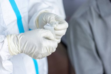PPE giysisi olan doktor, nazal çubuk ile ATK test kiti kullanan bir test koronavirüsü (covid-19) kullanıyor..
