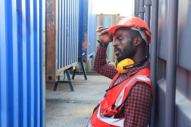 Afrikalı Amerikalı yakışıklı bir siyahi mühendisin yakınında lojistik taşımacılık ithalat veya nakliye endüstrisinin konteynır deposunda çalışıyor. 