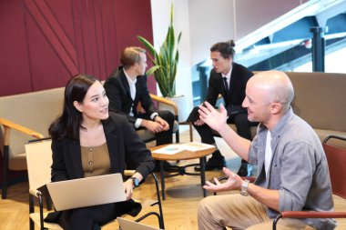 İş dünyasında çalışan ve iletişim kuran bir grup genç insan arka planda oturan meslektaşlarıyla birlikte ofis masasında oturuyorlar. Modern Ofis Toplantı Odası Yöneticileri ve Yatırımcılar Konuşuyor 