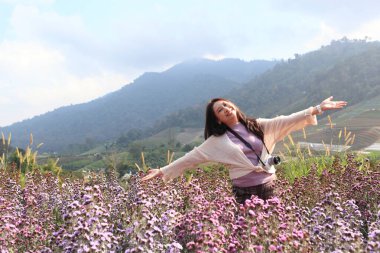 Kadın, sabah sisli havada pembe çiçeklerle dağlarla rahatlar. Romantik bir an yaşarlar.