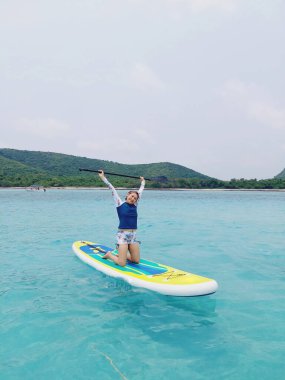  Sörf tahtasında dinlenen, turkuaz deniz suyunda yüzen bir kadın. Ayağa kalk Paddle bordası. Yaz eğlencesi, tatil seyahati. Etkin yaşam biçimi