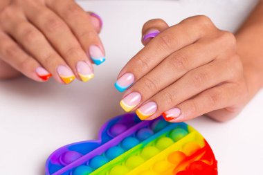 Renkli manikür tırnaklı güzel kadın elleri oyuncağı tutuyor, patlat.