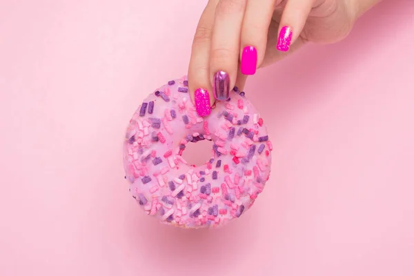 有粉色指甲的雌性手 上面挂着甜草莓甜甜圈 — 图库照片