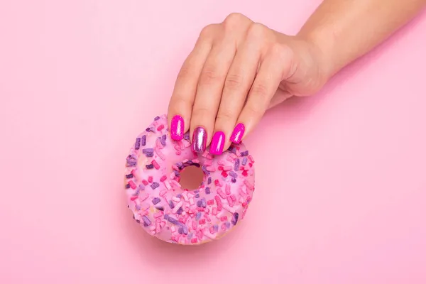 Pembe manikür tırnaklı, elinde tatlı çilekli çörek tutan bir kadın eli.
