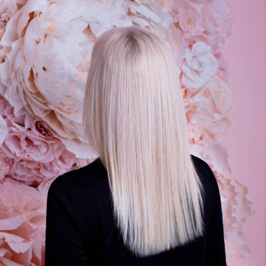 Uzun, düz, sağlıklı, sarı saçlı, siyah elbiseli, çiçek arkaplanda bir kadın.