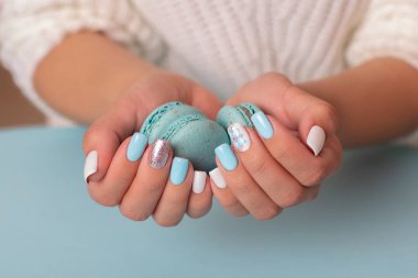 Mavi manikür tırnaklı kadın elleri tatlı badem kurabiyeleri tutuyor.