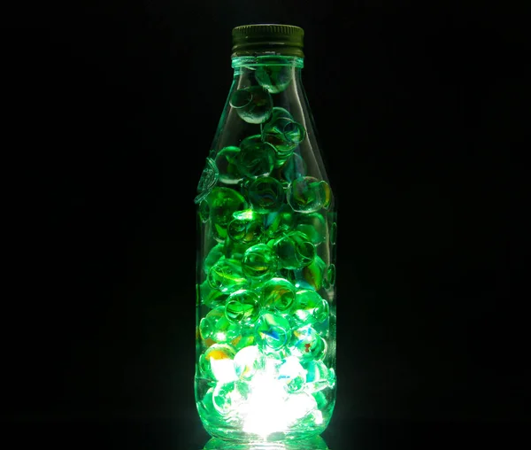 暗い背景にライト付きボトルの中にガラスのビー玉のクローズアップショット — ストック写真