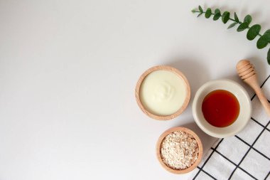Ev yapımı yüz maskesi için doğal malzemeler, beyaz arka planda yoğurt, yulaf ve bal manzarası, güzellik ürünleri konsepti, düz yatak.