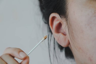 Beyaz arka planda pamuk tomurcuğuyla kulak temizleyen kadın.